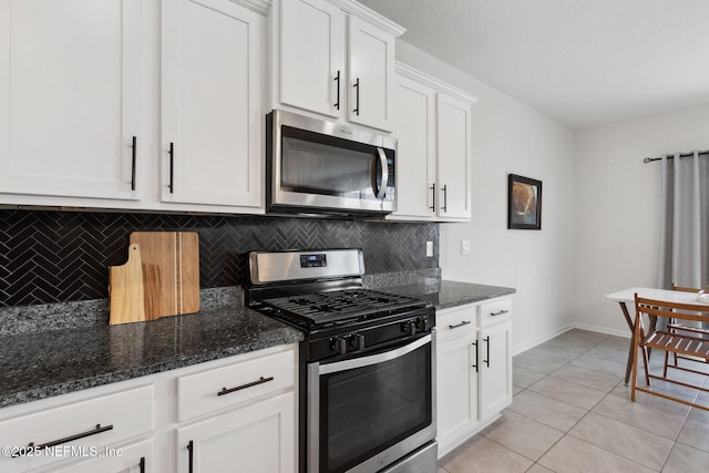 kitchen with dark stone countertops, stainless steel appliances, tasteful backsplash, white cabinets, and light tile patterned flooring