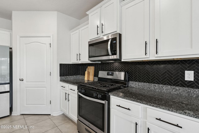 kitchen featuring appliances with stainless steel finishes, white cabinetry, tasteful backsplash, light tile patterned flooring, and dark stone counters