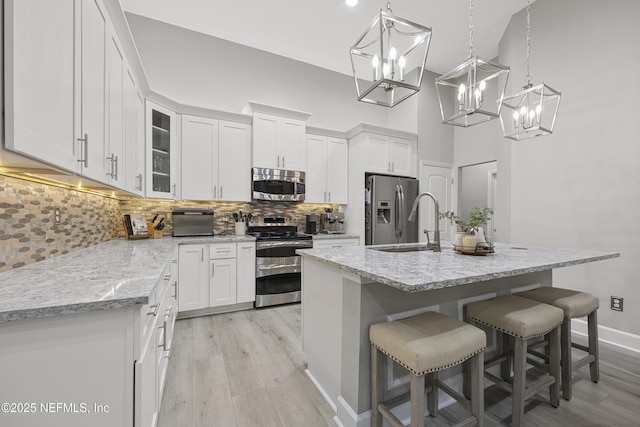 kitchen featuring stainless steel appliances, decorative light fixtures, a center island with sink, and white cabinets