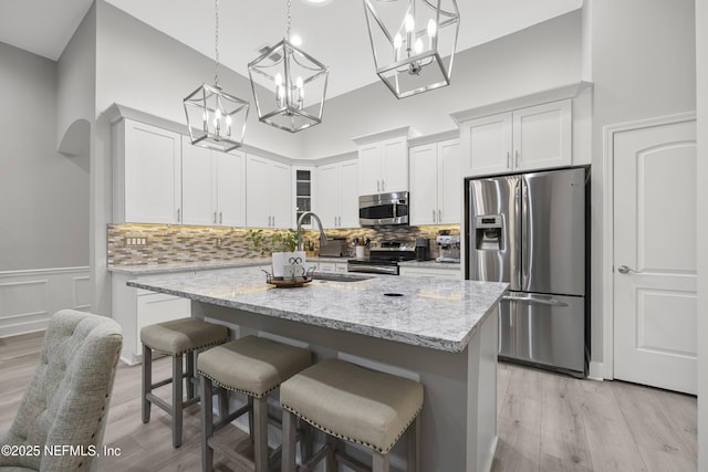 kitchen featuring white cabinetry, hanging light fixtures, light stone counters, and stainless steel appliances