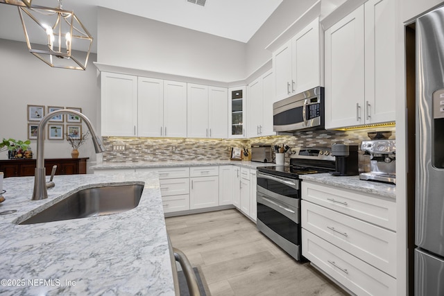 kitchen featuring pendant lighting, white cabinetry, sink, light stone counters, and stainless steel appliances