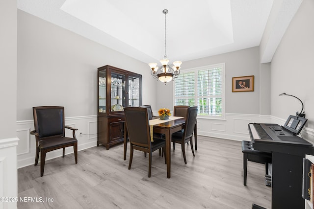 dining area featuring a notable chandelier, a tray ceiling, and light hardwood / wood-style flooring