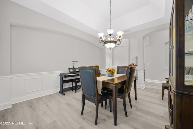 dining space with a tray ceiling, light hardwood / wood-style floors, and a notable chandelier