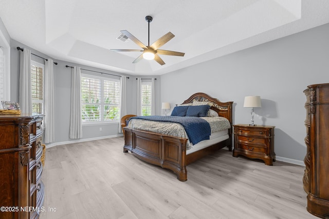 bedroom featuring a tray ceiling, light hardwood / wood-style floors, ceiling fan, and a textured ceiling