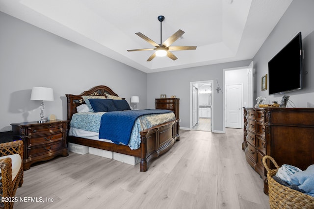 bedroom featuring ceiling fan, ensuite bath, a raised ceiling, and light hardwood / wood-style flooring