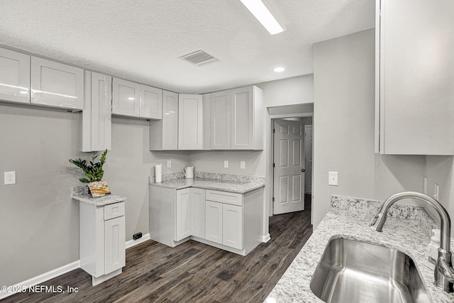 kitchen with light stone counters, dark wood-type flooring, sink, and white cabinets