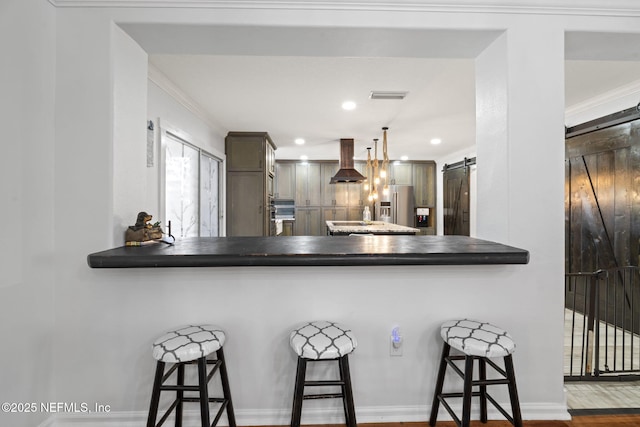 kitchen featuring kitchen peninsula, ventilation hood, a kitchen bar, stainless steel fridge with ice dispenser, and a barn door