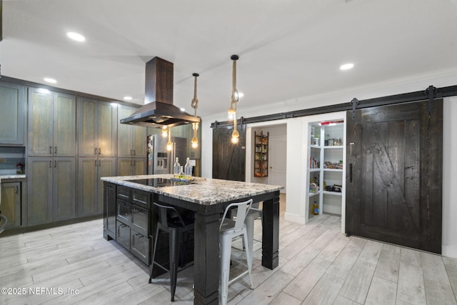 kitchen featuring a breakfast bar, pendant lighting, island exhaust hood, a barn door, and a kitchen island with sink