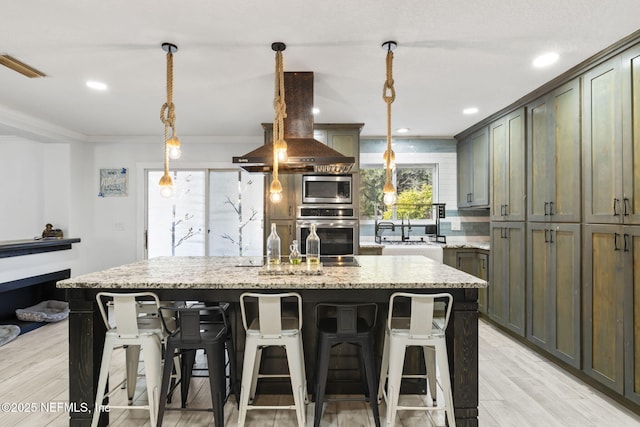 kitchen with appliances with stainless steel finishes, island range hood, pendant lighting, light stone countertops, and a center island with sink