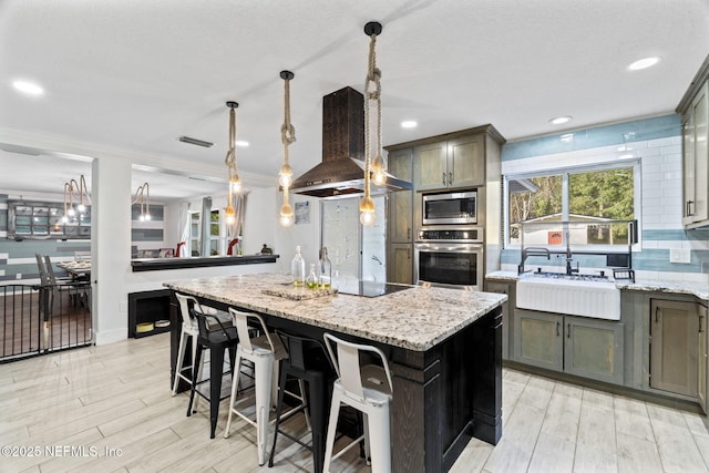 kitchen with pendant lighting, stainless steel appliances, a center island, light stone counters, and island exhaust hood