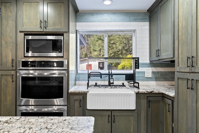 kitchen with tasteful backsplash, light stone countertops, appliances with stainless steel finishes, and sink