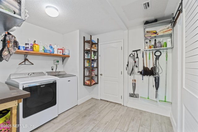 clothes washing area with a textured ceiling, a barn door, washing machine and clothes dryer, and light wood-type flooring