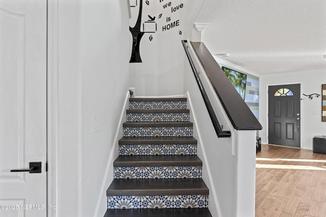 staircase with hardwood / wood-style flooring, ornamental molding, and a textured ceiling