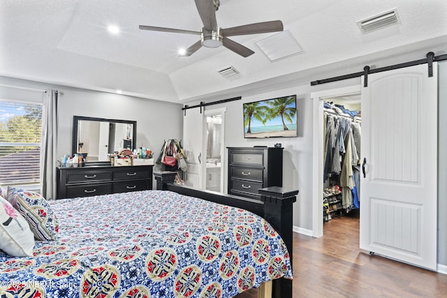 bedroom featuring hardwood / wood-style floors, a spacious closet, a tray ceiling, a barn door, and a textured ceiling