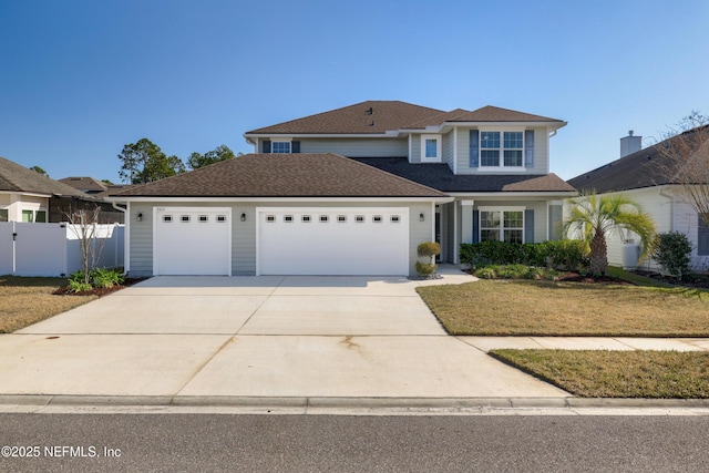 traditional-style house featuring driveway, a garage, roof with shingles, fence, and a front yard