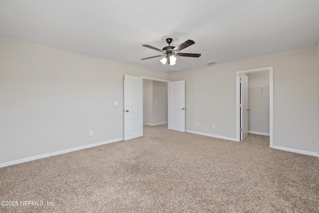 unfurnished bedroom featuring carpet floors, a ceiling fan, visible vents, baseboards, and a walk in closet