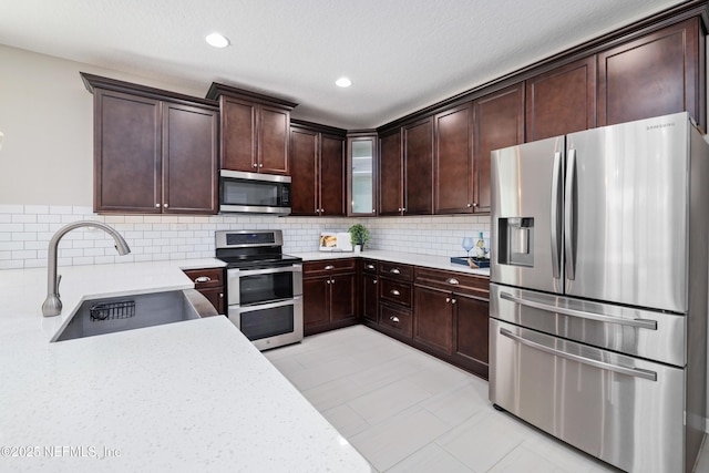 kitchen featuring sink, tasteful backsplash, dark brown cabinets, stainless steel appliances, and light stone countertops