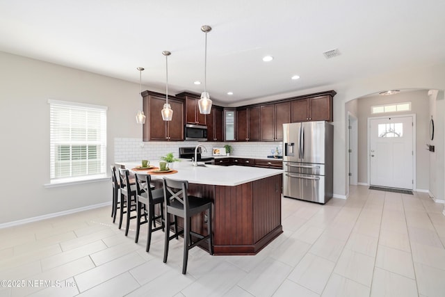 kitchen featuring arched walkways, decorative backsplash, appliances with stainless steel finishes, a peninsula, and dark brown cabinets