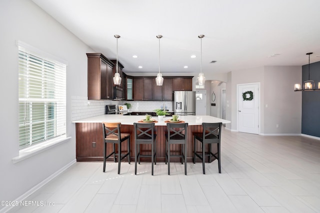 kitchen with appliances with stainless steel finishes, a breakfast bar, decorative light fixtures, tasteful backsplash, and kitchen peninsula