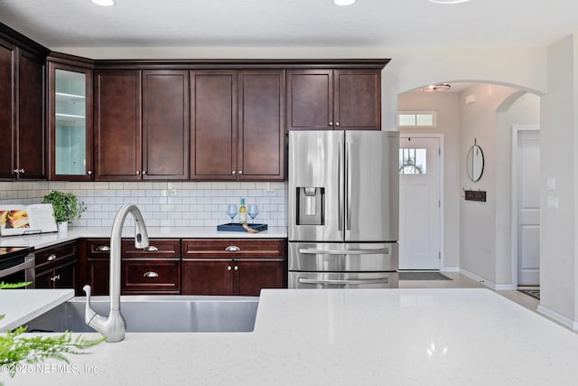 kitchen featuring arched walkways, tasteful backsplash, stainless steel refrigerator with ice dispenser, and a sink