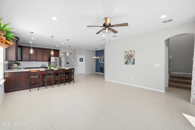 kitchen with pendant lighting, ceiling fan, dark brown cabinetry, stainless steel fridge with ice dispenser, and decorative backsplash