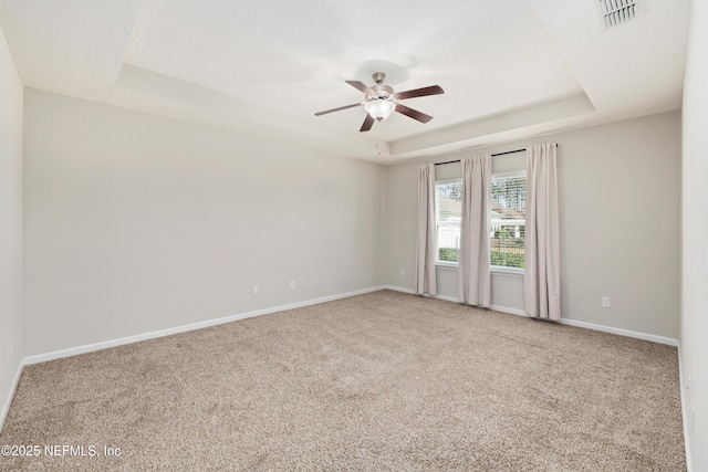 carpeted empty room featuring a ceiling fan, a raised ceiling, visible vents, and baseboards