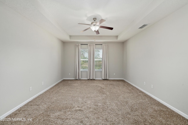 carpeted empty room featuring a ceiling fan, a raised ceiling, visible vents, and baseboards