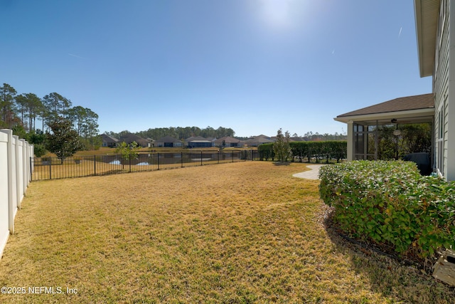 view of yard featuring a sunroom, a fenced backyard, and a water view