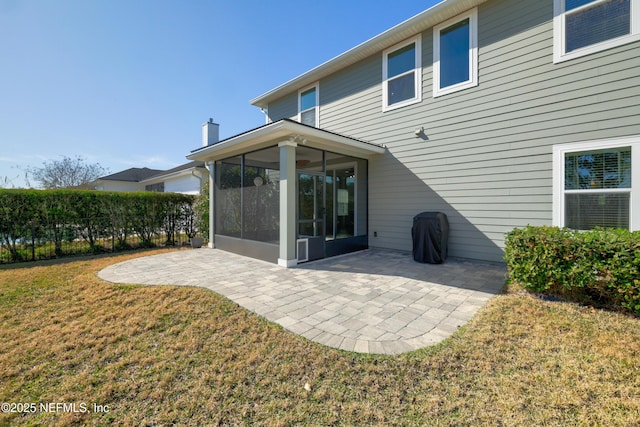 rear view of house featuring a chimney, a lawn, a sunroom, a patio area, and fence