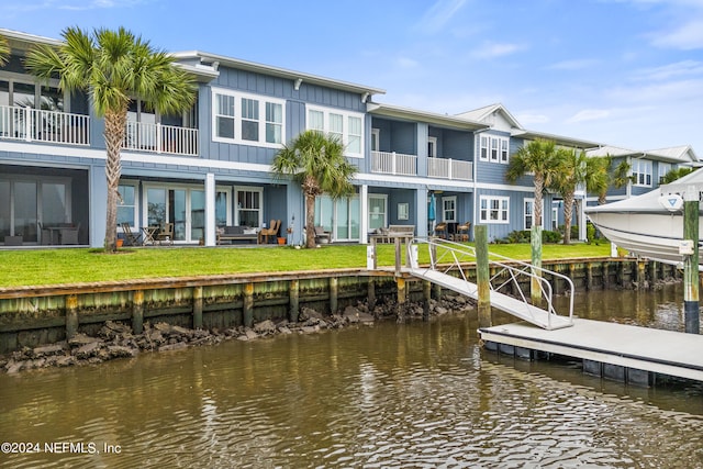 rear view of house featuring a balcony, a water view, and a lawn