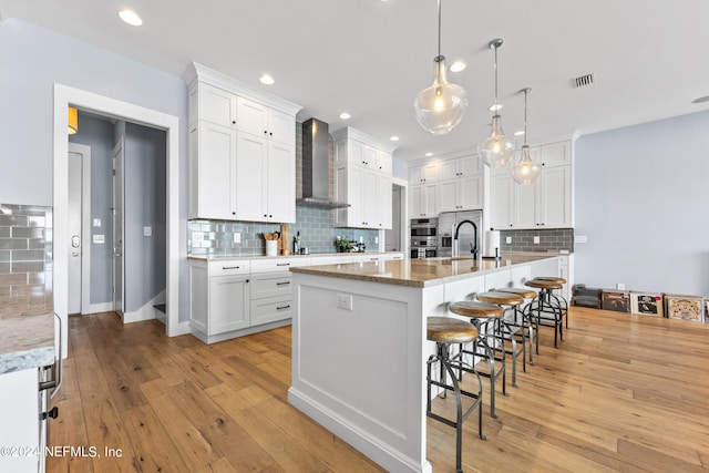 kitchen with light stone counters, wall chimney range hood, a large island, and white cabinets