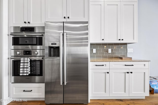 kitchen featuring white cabinetry, appliances with stainless steel finishes, light stone counters, and backsplash