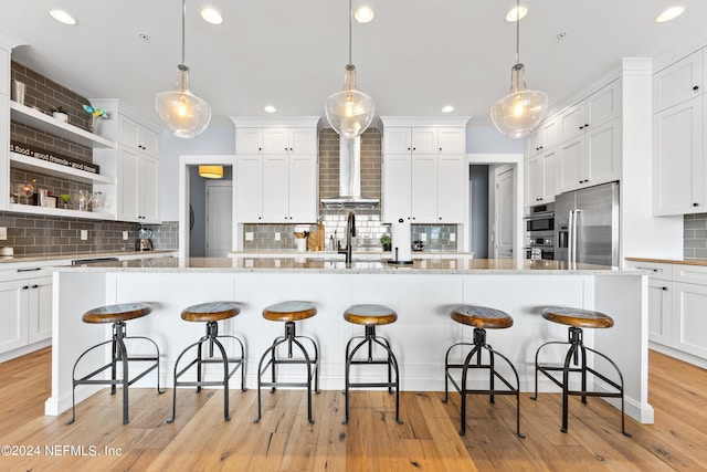 kitchen with appliances with stainless steel finishes, wall chimney exhaust hood, and a center island with sink