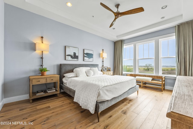 bedroom with a raised ceiling, ceiling fan, and light hardwood / wood-style floors