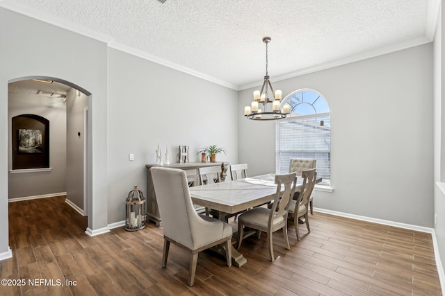 dining area featuring crown molding, wood-type flooring, a textured ceiling, and a notable chandelier