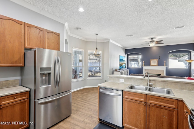 kitchen featuring pendant lighting, sink, light hardwood / wood-style flooring, appliances with stainless steel finishes, and a tiled fireplace