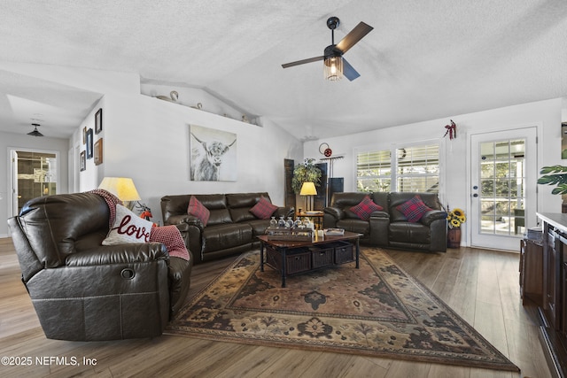 living room with vaulted ceiling, ceiling fan, a textured ceiling, and light hardwood / wood-style flooring