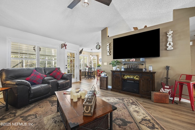 living room with hardwood / wood-style flooring, vaulted ceiling, ceiling fan, and a textured ceiling