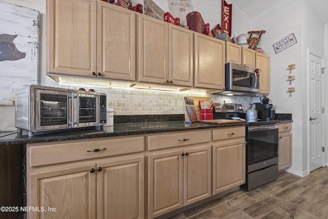 kitchen with hardwood / wood-style floors, dark stone countertops, backsplash, stainless steel appliances, and light brown cabinets