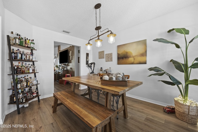 dining room with dark hardwood / wood-style flooring, a textured ceiling, and bar area