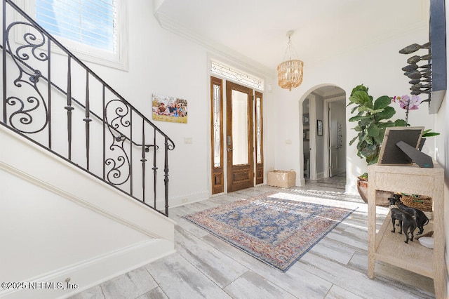 foyer entrance with arched walkways, wood finished floors, stairs, an inviting chandelier, and crown molding