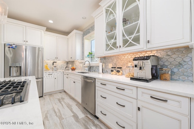 kitchen featuring stainless steel appliances, light countertops, glass insert cabinets, and a sink