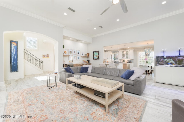 living area featuring arched walkways, ceiling fan with notable chandelier, visible vents, ornamental molding, and stairway