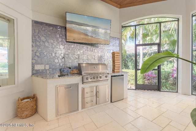 kitchen featuring light stone counters, freestanding refrigerator, stone tile flooring, and tasteful backsplash