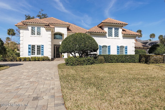 mediterranean / spanish home featuring a tile roof, a front lawn, and stucco siding