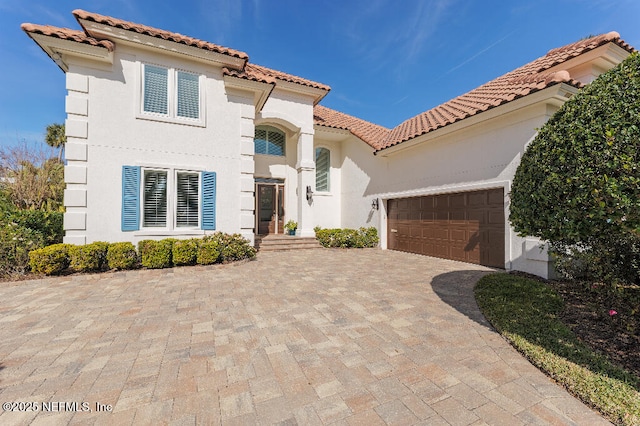 mediterranean / spanish house with decorative driveway, a tile roof, an attached garage, and stucco siding