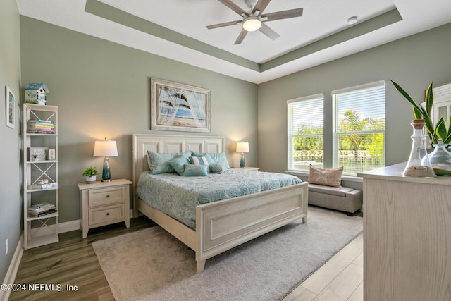 bedroom with ceiling fan, a raised ceiling, and hardwood / wood-style floors