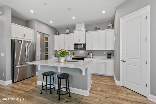 kitchen featuring light hardwood / wood-style flooring, a breakfast bar, white cabinetry, a kitchen island with sink, and stainless steel appliances