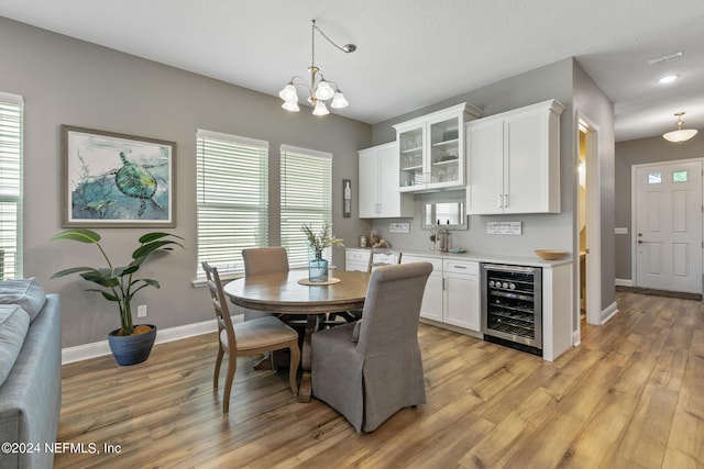 dining area featuring an inviting chandelier, beverage cooler, sink, and light hardwood / wood-style flooring