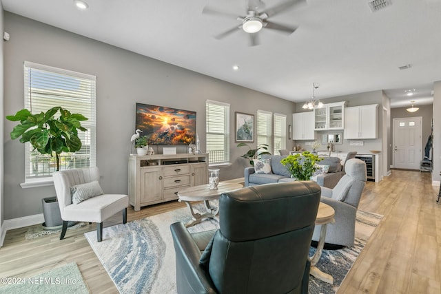 living room with a healthy amount of sunlight, ceiling fan with notable chandelier, beverage cooler, and light hardwood / wood-style flooring